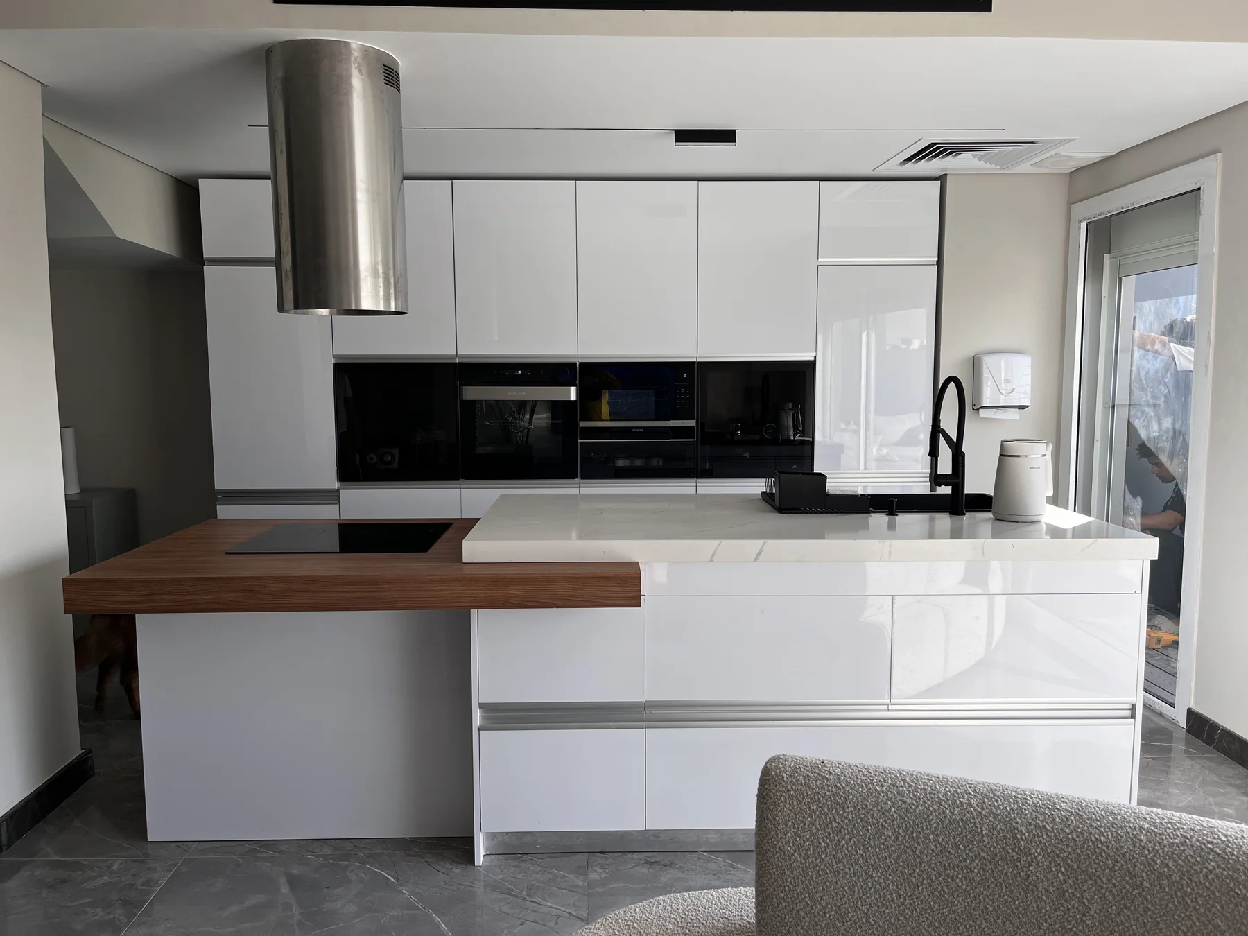 Wide view of a glossy white kitchen with a walnut counter